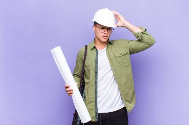 Genç sarışın adam şaşkın ve şaşkın hissediyor, başını kaşıyor ve yan tarafa bakıyor.