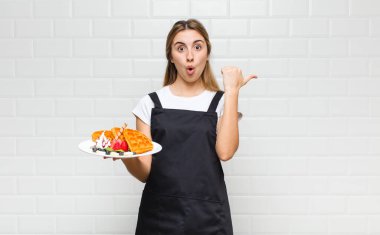 Sarışın, güzel bir kadın inançsızlıktan şaşkın şaşkın bakıyor, yan taraftaki objeyi işaret ediyor ve 