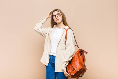 Sarışın, güzel bir kadın kafası karışık ve kafası karışık, başını kaşıyor ve yan tarafa bakıyor.