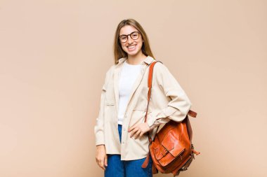 Sarışın, güzel bir kadın mutlu bir şekilde gülümsüyor, eli kalçasında ve kendinden emin, olumlu, gururlu ve arkadaş canlısı.