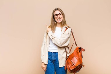 Sarışın, güzel bir kadın neşeli bir şekilde gülümsüyor, mutlu hissediyor ve kenarı ve yukarıyı işaret ediyor, fotokopi uzayındaki nesneleri gösteriyor.