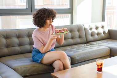 Genç ve güzel bir kadın yeni evinde sandviç yiyor.