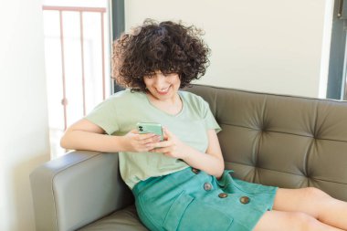 Genç ve güzel bir kadın yeni evinde akıllı telefonunu kullanıyor.