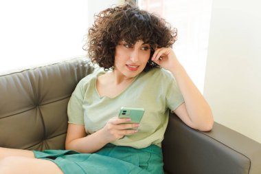 Genç ve güzel bir kadın yeni evinde akıllı telefonunu kullanıyor.