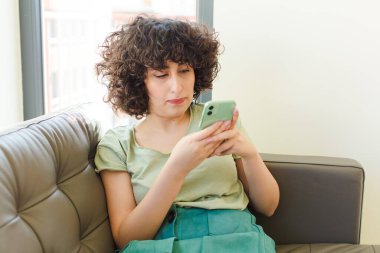 Genç ve güzel bir kadın yeni evinde akıllı telefonunu kullanıyor.