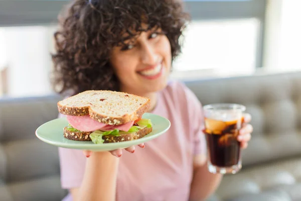 young pretty woman eating a sandwich with a cola drink