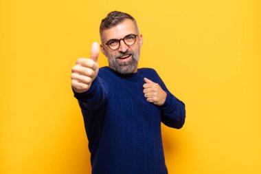 Yetişkin, yakışıklı, gururlu, tasasız, kendinden emin ve mutlu, başparmaklarıyla gülümseyen bir adam.