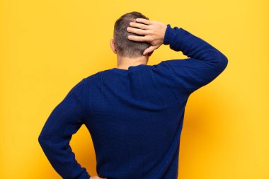 Yetişkin yakışıklı bir adam düşünüyor ya da şüphe ediyor, kafasını kaşıyor, kafası karışık ve kafası karışık hissediyor, geriye ya da arkaya bakıyor.