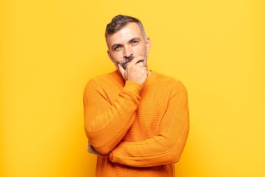 Yetişkin yakışıklı adam ciddi görünüyor, kafası karışık, kararsız ve düşünceli, seçenekler ve seçenekler arasında şüpheci.