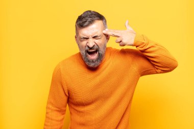 Yetişkin yakışıklı adam mutsuz ve stresli görünüyor, intihar jesti elle silah işareti yapıyor, kafasını işaret ediyor.