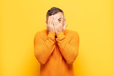 Yetişkin, yakışıklı bir adam korkmuş ya da utanmış hissediyor. Gözleri yarı kapalı ya da elleri kapalı gözetliyor.