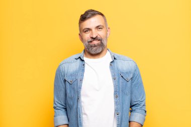 Olumlu, mutlu, kendinden emin ve rahat bir ifadeyle neşeli ve rahat gülümseyen yetişkin bir adam.