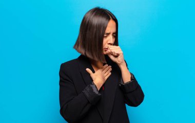 Boğazı ağrıyan ve grip belirtileri gösteren ağzı kapalı öksüren İspanyol bir kadın.