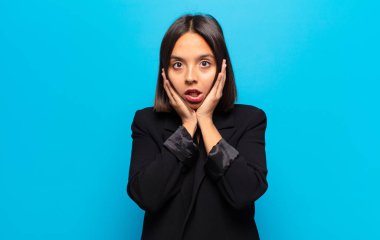 İspanyol kadın şok olmuş ve korkmuş hissediyor, ağzı açık ve elleri yanaklarında korkmuş görünüyor.