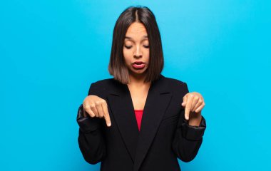 İki eliyle aşağıya bakan ağzı açık İspanyol bir kadın. Şok olmuş, şaşırmış ve şaşırmış görünüyor.