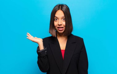 İspanyol kadın şaşırmış ve şoka uğramış görünüyor, çenesi düşmüş, eli açık bir objeyi tutuyor.