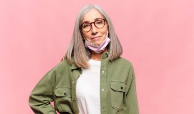 Orta yaşlı bir kadın mutlu bir şekilde gülümsüyor. Kendine güvenen, olumlu, gururlu ve arkadaş canlısı bir tavırla.