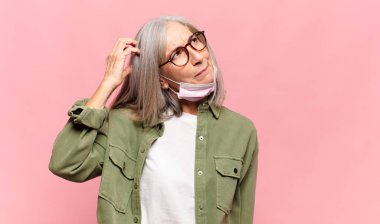 Orta yaşlı kadın şaşkın ve şaşkın hissediyor, kafasını kaşıyor ve yan tarafa bakıyor.