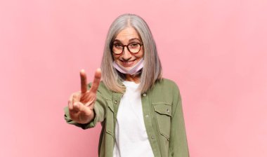 Orta yaşlı bir kadın gülümsüyor ve arkadaş canlısı görünüyor. İki ya da iki numarayı gösteriyor. Elleri önde, geriye doğru sayıyor.