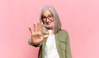 Orta yaşlı bir kadın gülümsüyor ve arkadaş canlısı görünüyor. 5 ya da 5 numarayı gösteriyor.