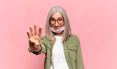 Orta yaşlı bir kadın gülümsüyor ve arkadaş canlısı görünüyor. Elleri önde, geriye doğru sayıyor.