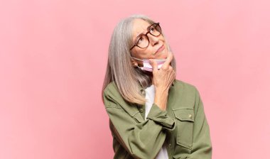 Orta yaşlı kadın düşünüyor, kuşkulu ve şaşkın hissediyor, farklı seçeneklerle, hangi kararı vereceğini merak ediyor.