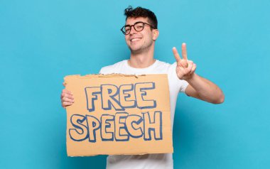 Genç adam gülümsüyor ve mutlu görünüyor, kaygısız ve pozitif, tek elle zafer ya da barış işareti yapıyor.