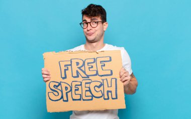 Genç adam omuz silkiyor, kafası karışık ve kararsız, kolları bağlı ve şaşkın bir şekilde şüpheli bakıyor.