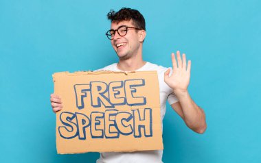 Genç adam mutlu ve neşeyle gülümsüyor, el sallıyor, seni selamlıyor ve selamlıyor, ya da hoşça kal diyor.