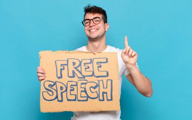 Genç adam gülümsüyor ve arkadaş canlısı görünüyor, bir numarayı gösteriyor ya da ilk eli önde, geriye doğru sayıyor.