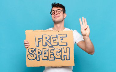 Genç adam gülümsüyor ve arkadaş canlısı görünüyor, üç ya da üç numarayı gösteriyor, eli önde, geriye doğru sayıyor.