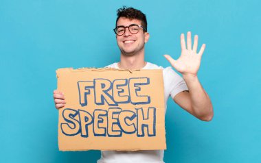 Genç adam gülümsüyor ve arkadaş canlısı görünüyor, 5 ya da 5 numarayı gösteriyor, eli önde, geriye doğru sayıyor.