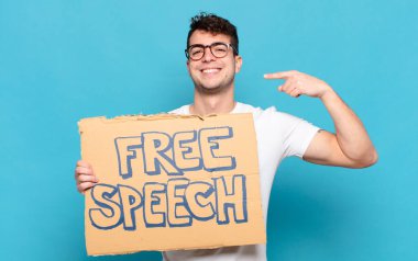 Genç adam kendinden emin bir şekilde gülümseyerek kendi geniş gülüşünü, pozitif, rahat, tatmin olmuş tavrını gösteriyor.