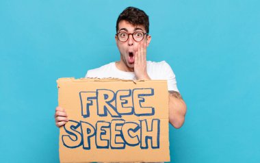 Genç adam şok olmuş ve korkmuş hissediyor, ağzı açık ve elleri yanaklarında korkmuş görünüyor.