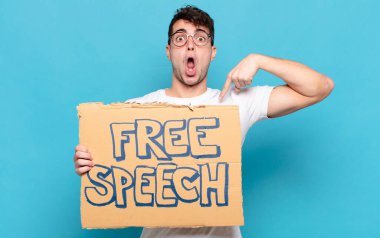 Şok olmuş ve ağzı açık, kendini işaret eden genç bir adam.