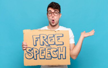 Genç adam şaşırmış ve şok olmuş görünüyor, çenesi düşmüş bir nesneyi elinde açık bir elle tutuyor.