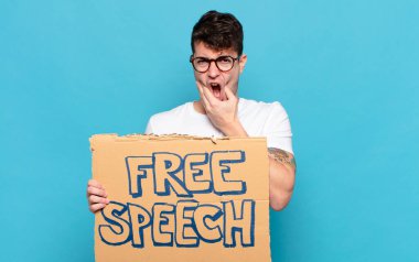 Ağzı ve gözleri açık, eli çenesinde olan genç bir adam, nahoş bir şekilde şokta, ne ya da vay canına diyor.