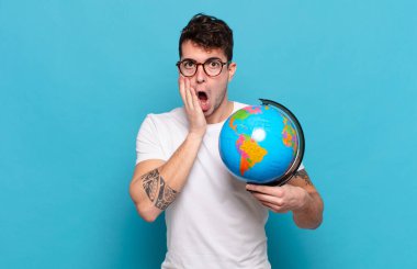 Genç adam şok olmuş ve korkmuş hissediyor, ağzı açık ve elleri yanaklarında korkmuş görünüyor.