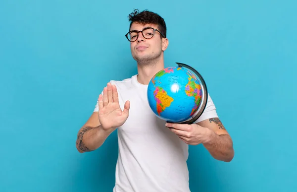 young man looking serious, stern, displeased and angry showing open palm making stop gesture