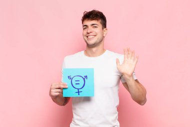 Genç adam mutlu ve neşeyle gülümsüyor, el sallıyor, seni selamlıyor ve selamlıyor, ya da hoşça kal diyor.