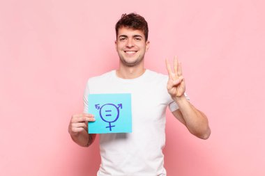 Genç adam gülümsüyor ve arkadaş canlısı görünüyor, üç ya da üç numarayı gösteriyor, eli önde, geriye doğru sayıyor.