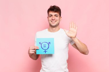 Genç adam gülümsüyor ve arkadaş canlısı görünüyor, 5 ya da 5 numarayı gösteriyor, eli önde, geriye doğru sayıyor.