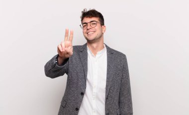 Genç adam gülümsüyor ve mutlu görünüyor, kaygısız ve pozitif, tek elle zafer ya da barış işareti yapıyor.