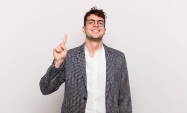 Genç adam gülümsüyor ve arkadaş canlısı görünüyor, bir numarayı gösteriyor ya da ilk eli önde, geriye doğru sayıyor.