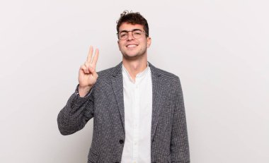 Genç adam gülümsüyor ve arkadaş canlısı görünüyor, iki ya da iki numarayı gösteriyor, elleri önde, geriye doğru sayıyor.