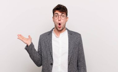 Genç adam şaşırmış ve şok olmuş görünüyor, çenesi düşmüş bir nesneyi elinde açık bir elle tutuyor.