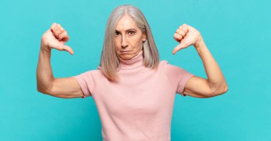 Orta yaşlı bir kadın üzgün, hayal kırıklığına uğramış ya da kızgın görünüyor. Anlaşmazlıkta baş parmağını gösteriyor. Hayal kırıklığına uğramış hissediyor.