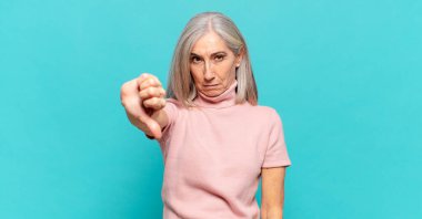 Orta yaşlı bir kadın sinirli, sinirli, hayal kırıklığına uğramış ya da canı sıkkın, ciddi bir bakışla başparmağını kaldırıyor.