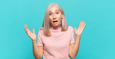 Orta yaşlı bir kadın mutlu, heyecanlı, şaşırmış ya da şaşırmış hissediyor, gülümsüyor ve hayret verici bir şeye şaşırıyor.