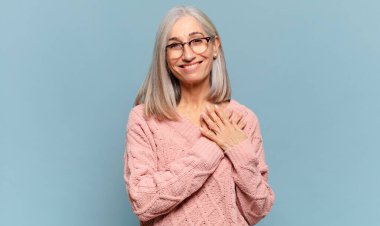 Orta yaşlı bir kadın romantik, mutlu ve aşık, neşeli bir şekilde gülümseyen ve kalbe yakın el ele tutuşan